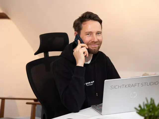Dirk Grüner telefoniert am Schreibtisch, im Hintergrund der Laptop mit Sichtkraft-Studio-Aufkleber
